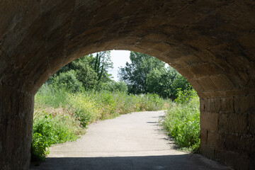 A walk path surrounded by greenery crosses a tunnel