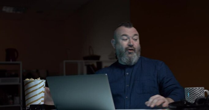 A man enthusiastically starts watching a movie on his laptop and takes first a small bucket of popcorn and then a large one. A funny situation