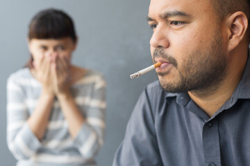 Husband smoking cigarette and wife choking of smoke. Man smoking cigarette and woman is covering...