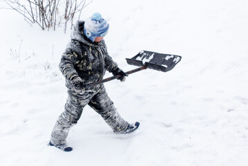Fototapeta na wymiar A boy with a shovel cleans snow