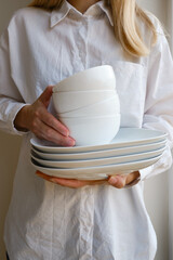 A woman is holding a stack of white clean dishes. Plates close up