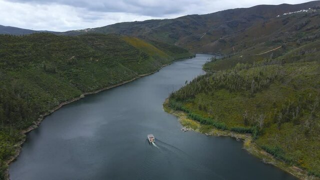 Aerial view of a Solar Boat sailing through the valleys os Z&ecirc;zere river in Portugal on a cloudy day. Amazing pine wood forest.