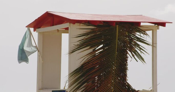 Flag Blowing In The Wind At Lifeguard Shack With Coconut Leaves At Balneario del Escambron, Beach In San Juan, Puerto Rico. - static shot