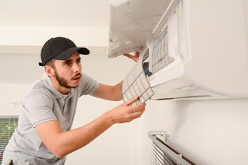 handsome young man electrician cleaning air filter on an indoor unit of air conditioning system in...