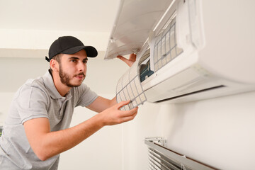 handsome young man electrician cleaning air filter on an indoor unit of air conditioning system in...