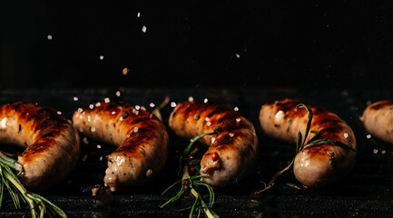 Grilled sausage bratwursts cooking on flaming grill BBQ grill sizzling over flaming hot coals. steel grilled meat. Long banner format - obrazy, fototapety, plakaty