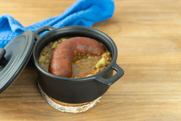Black pot with lentils and sausage on wooden background. Copy space.