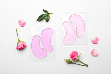 Packages with under eye patches and rose flowers on white background, flat lay. Cosmetic product