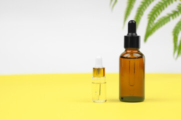 Two bottles with essential oils or serum for the face on a yellow background. Body care