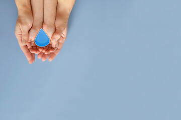 The hands of an adult and a child hold a drop on a blue background. The concept of water conservation.