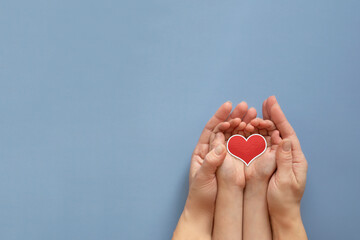 The hands of an adult and a child hold a heart on a blue background. The concept of health.