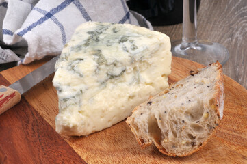 Morceau de fromage français à pâte persillée sur une planche à découper avec un couteau et des morceaux de pain en gros plan