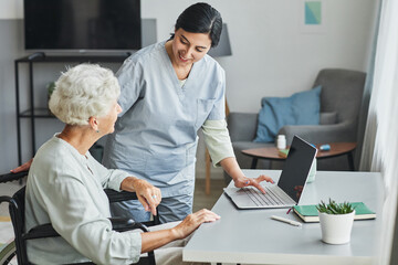Portrait of female caregiver assisting senior woman in wheelchair at home, copy space