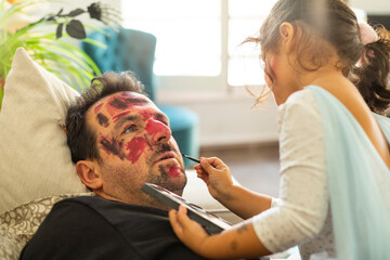 A little girl doing her father's Halloween makeup