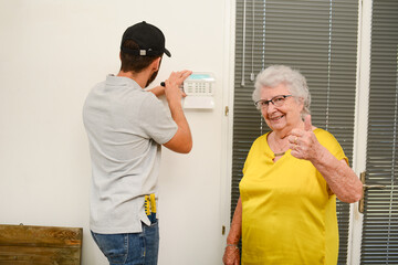 handsome young man installing house security anti burglary camera and siren alarm in a senior woman...