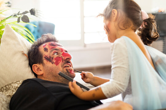 Beautiful daughter makes up her father lying on the sofa for the halloween party