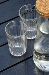 Two faceted glasses and a jug of drinking water stand on a black wooden table in a summer cafe