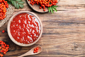 Flat lay composition with delicious rowan jam and berries on wooden table. Space for text