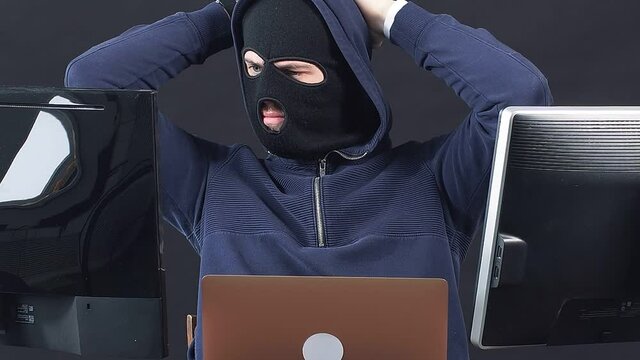 Hacker man in balaclava, sit in hood of pullover. Programmer male hiding face behind a mask, hack anonymously, man engaged in crime.