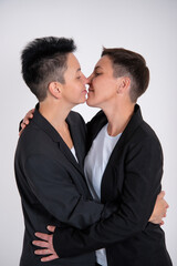 Two gay women are kissing on a gray background in business suits.
