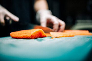 Close-up of hand sushi chef in gloves slices fresh salmon fish fillet at sushi bar.