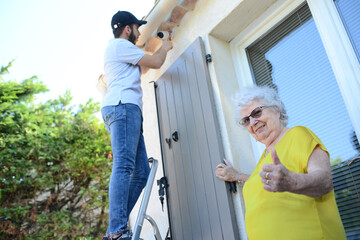 handsome young man installing house security anti burglary camera and siren alarm in a senior woman home