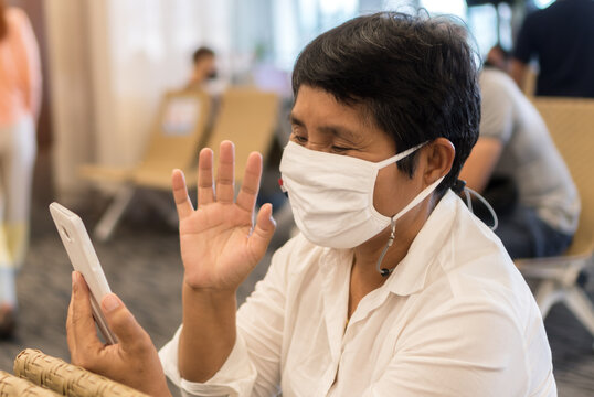 Asian Senior Traveler with New Normal in protecting face mask using smartphone for online social media reading news and searching check in flight timetable at airport terminal. Safe travel in COVID-19
