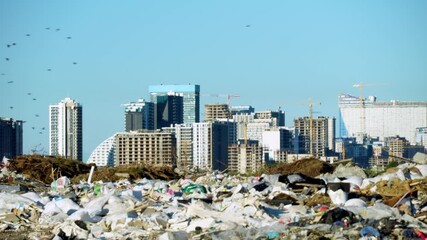Garbage dump. Skyscrapers, a construction site with a crane and houses of a big city in the background. concept of environmental pollution. Blue sky. The area of the city. flocks of birds are flying.