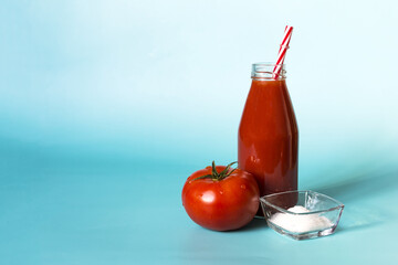Tomato juice in a transparent bottle, red tomato and salt in natural light on a blue background