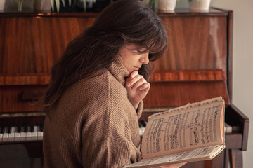 Fototapeta na wymiar Young woman musician looks into a collection of notes, sitting at the piano.