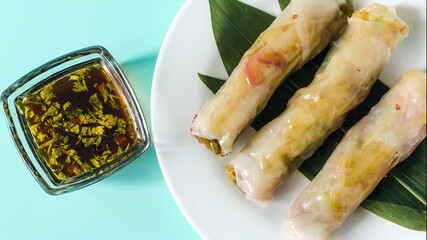 Spring rolls of seafood and vegetables with a decor of green leaves and dark sauce on a light background.