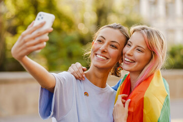 Young lesbian couple standing with rainbow flag - Powered by Adobe