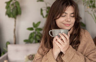 A young woman in a cozy sweater is enjoying a cup of drink.