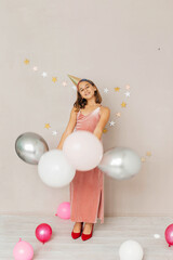 Fototapeta premium A beautiful teenager girl in an elegant pink dress, a festive cap and balloons celebrates her birthday.