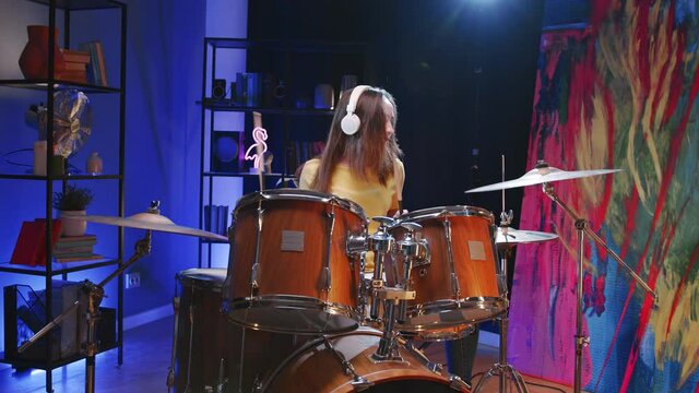 Waist up portrait view of the female musician wearing headphones plays drums while preparing to the concert. Music and hobbies concept