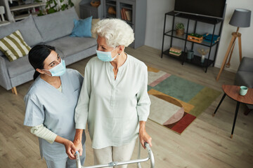 High angle portrait of smiling female nurse helping senior woman using mobility walker in retirement home, copy space
