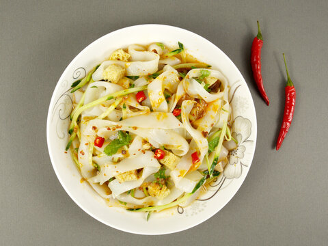 Cold skin noodles in a white bowl and red peppers, street food