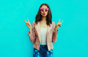 Portrait of beautiful young woman blowing her lips sending air kiss posing wearing a leather jacket...