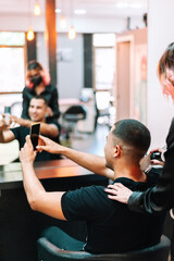 Man at hairdresser taking a selfie with a smartphone after getting a hair cut.