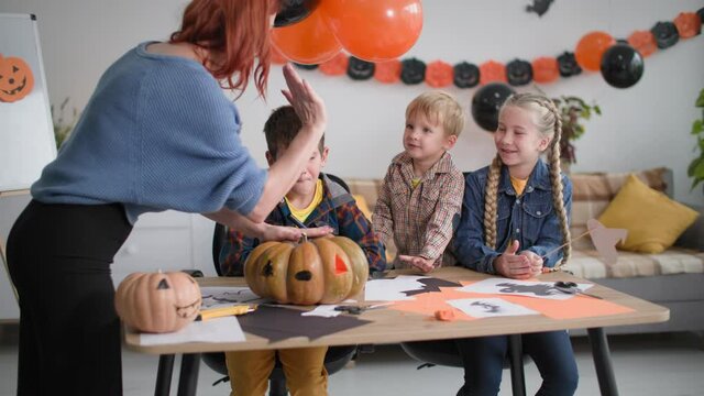 halloween for cute children at home, mother gives little son five and helps make decorations for holiday on the background of garlands in the shape of pumpkins