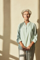 Vertical portrait of elegant senior woman looking at camera lit by sunlight against neutral background