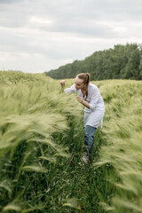 Naklejka na ściany i meble Young woman agronomist in white coat squatting in green wheat field and checking crop quality