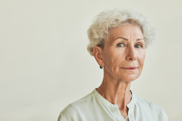 Close up portrait of elegant senior woman looking at camera while standing against neutral...