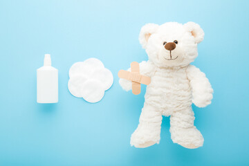 White bottle of hydrogen peroxide, cleansing cotton pads, adhesive bandages and fluffy teddy bear light blue background. Pastel color. Medical kit for skin wound cleaning of children. Top down view.