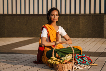 Young indian woman making namaste gesture while sitting on sidewalk