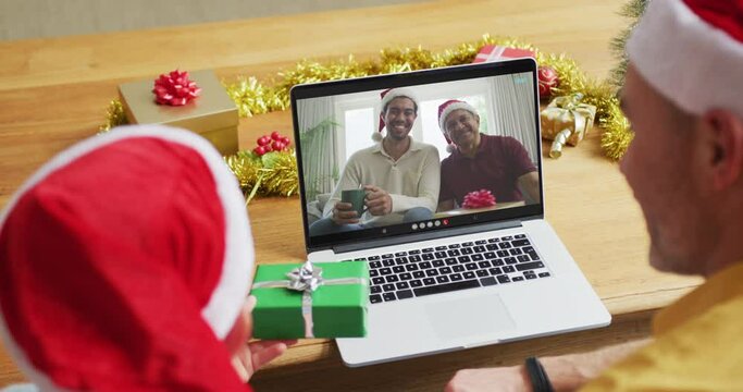 Caucasian father with son using laptop for christmas video call, with family on screen