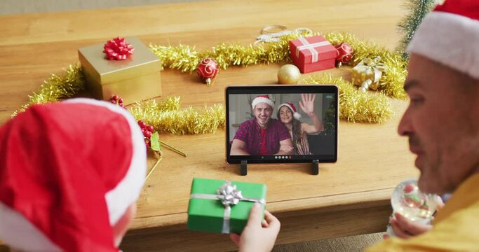 Caucasian father with son using tablet for christmas video call, with smiling friends on screen