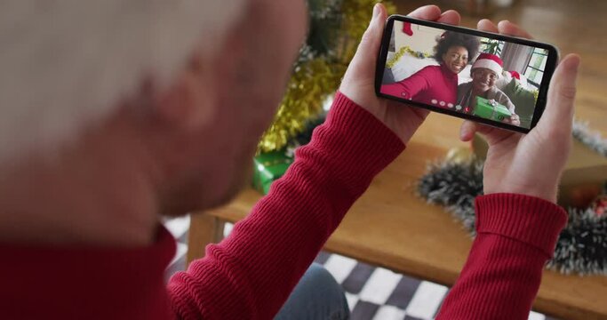 Caucasian man using smartphone for christmas video call, with smiling family on screen