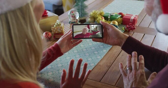 Caucasian couple with santa hats using smartphone for christmas video call with friend on screen
