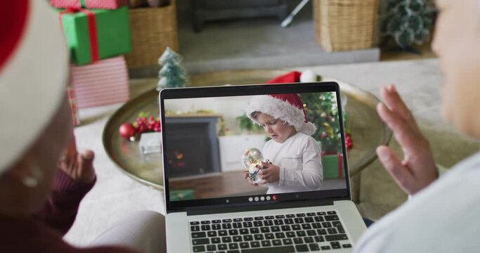 Senior diverse female friends using laptop for christmas video call with caucasian boy on screen